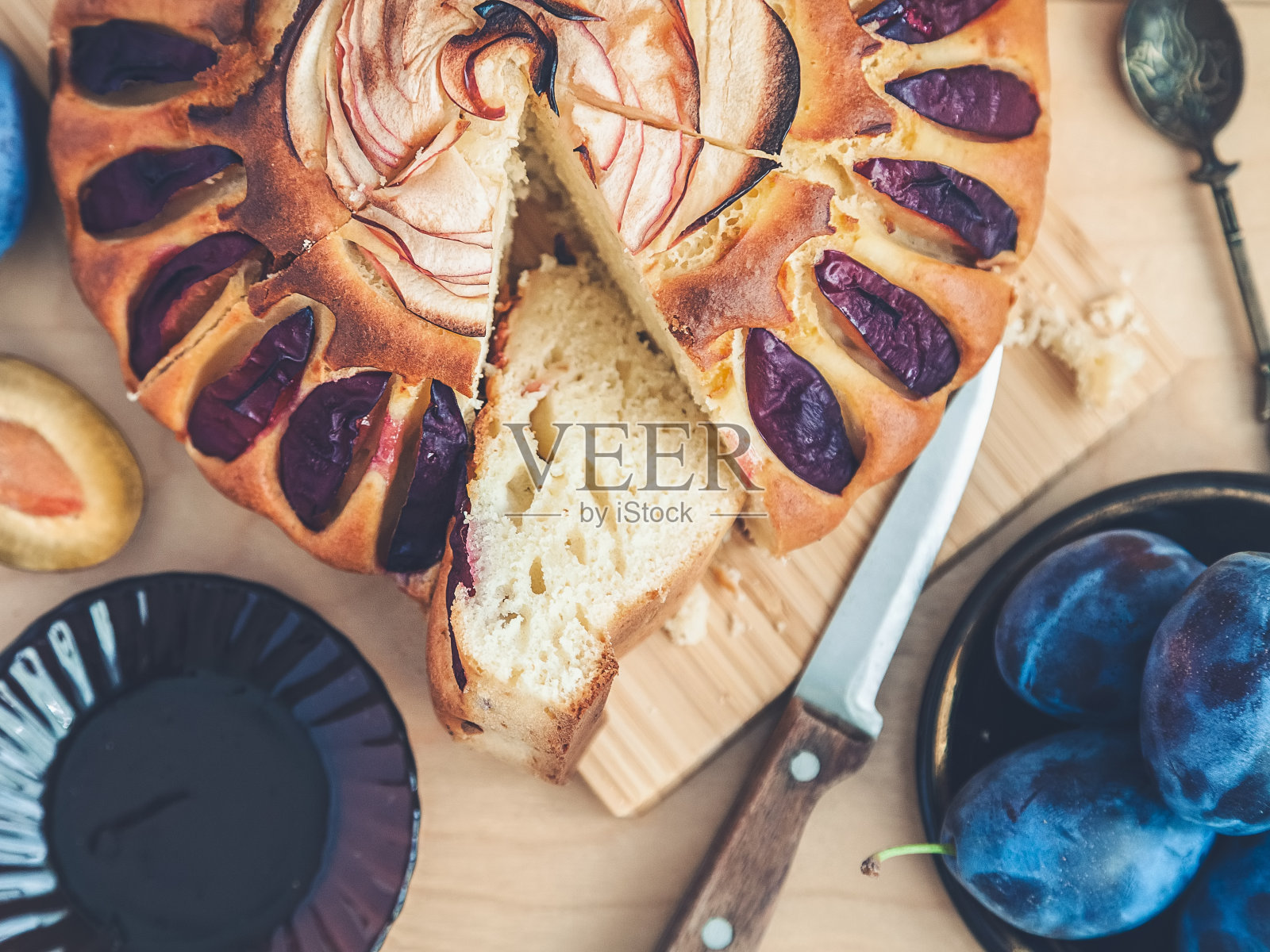 一个圆梅子蛋糕，切成片，点缀着一朵从苹果片上切下来的玫瑰，一杯红茶和一碟水果照片摄影图片