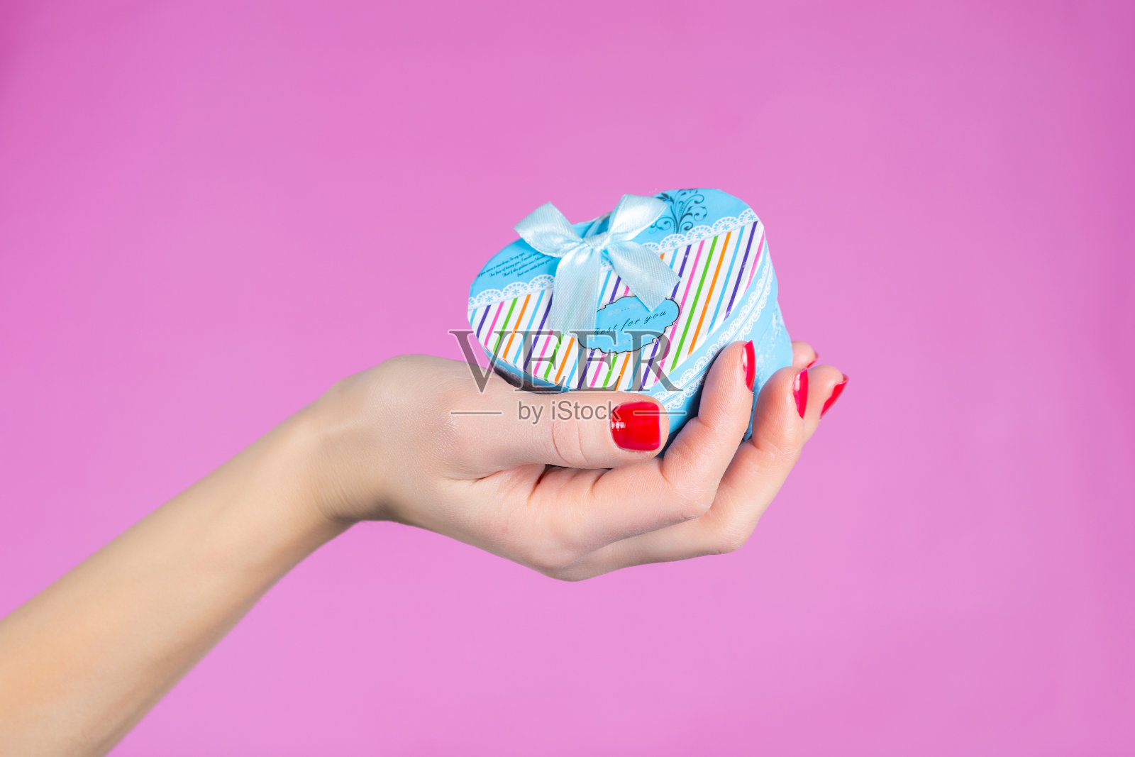 在工作室里，女性手拿着一个蓝色的心形礼盒，孤立在粉红色的背景上照片摄影图片