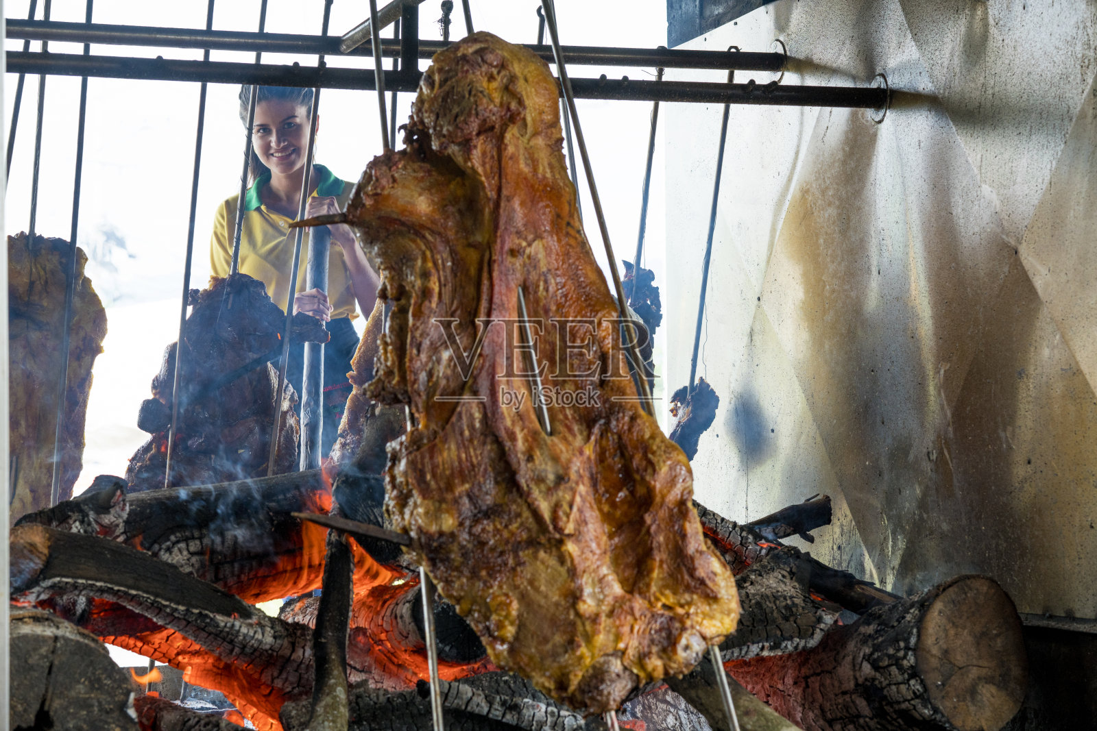 一位黑头发的拉丁妇女穿着黄色衬衫制服，制服上有黑色和黑色的细节，背景是一个典型的餐厅的女服务员，在一个大烤架上煮着典型的哥伦比亚肉，叫做mamona照片摄影图片