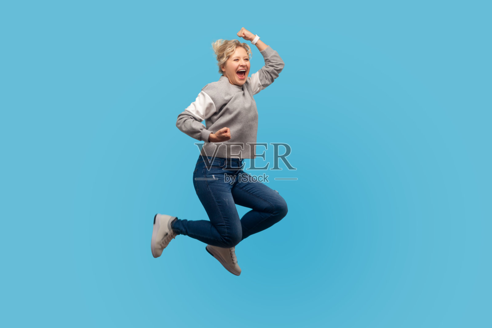 热情快乐的女人的肖像与短卷头发在运动衫跳在空中显示是的我做了它的手势照片摄影图片