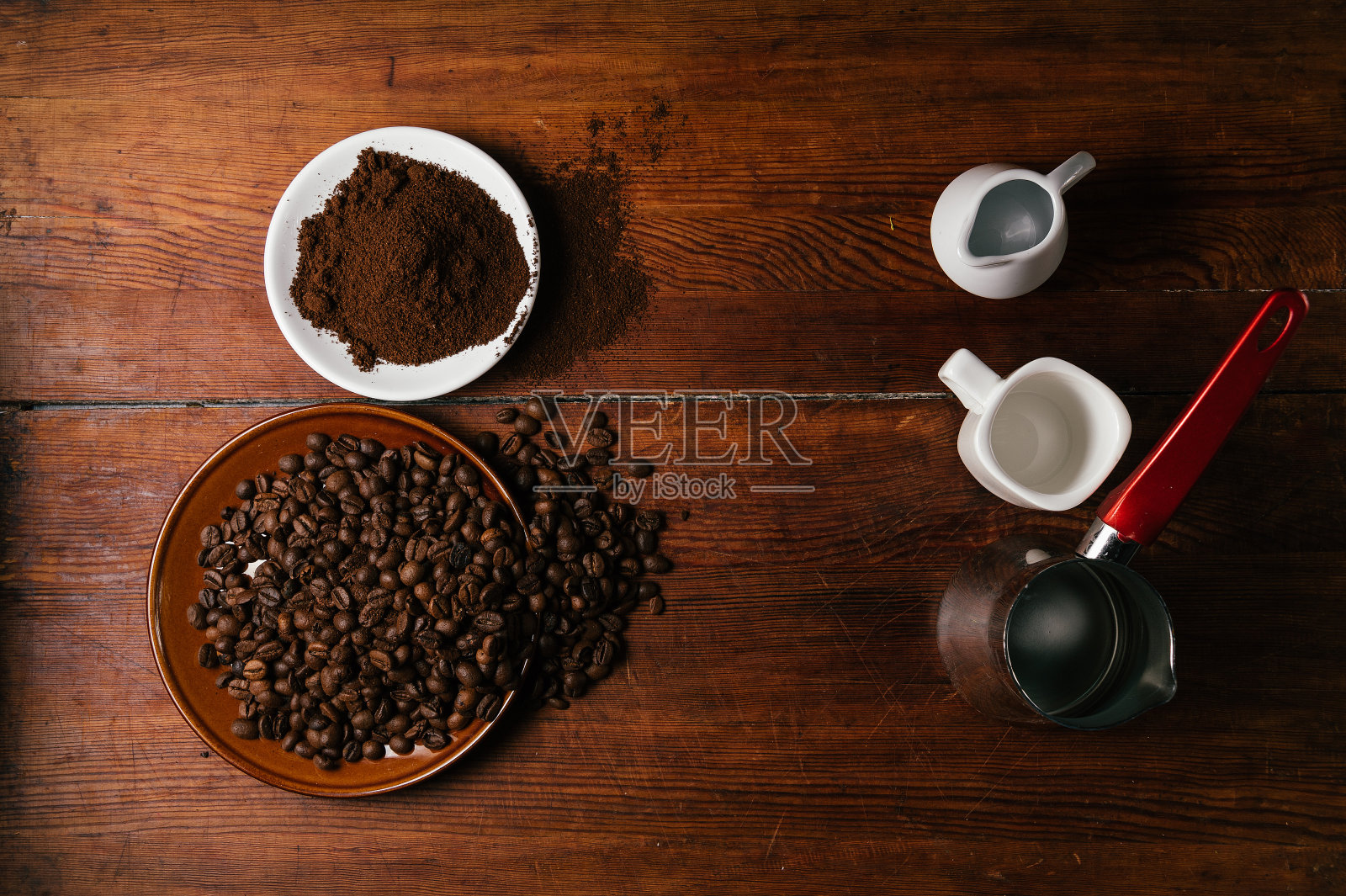 好的咖啡原料和工具。木桌上放着磨碎的咖啡豆。杯子，牛奶杯和用来煮咖啡的cezve。照片摄影图片