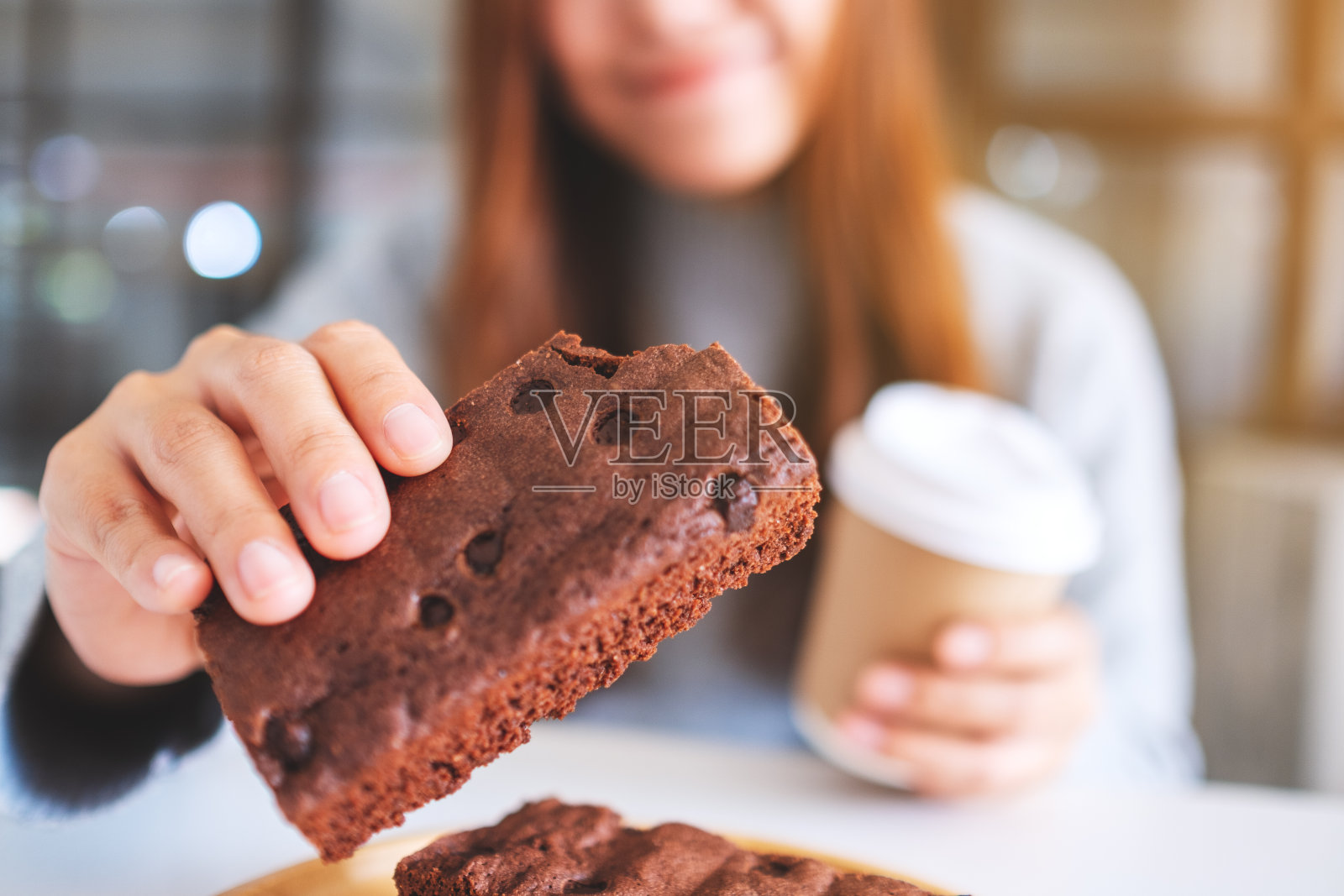 一位美丽的女人一边喝咖啡，一边拿着并吃着一块布朗尼蛋糕照片摄影图片