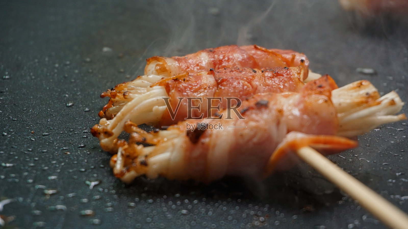 熏肉卷配金针菇放在烤盘上烤。照片摄影图片