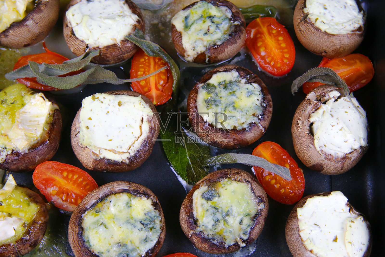靠近烤箱托盘白色香槟蘑菇填充软奶酪，西红柿和鼠尾草叶照片摄影图片