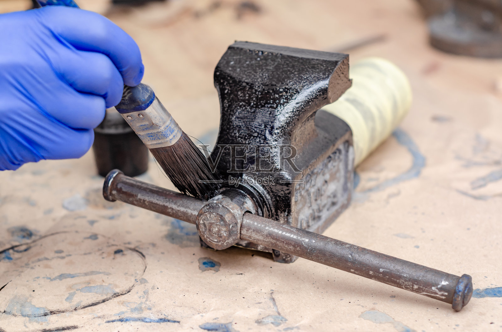 戴蓝色橡胶手套用刷子将黑色油漆涂在旧虎钳的金属部件上照片摄影图片