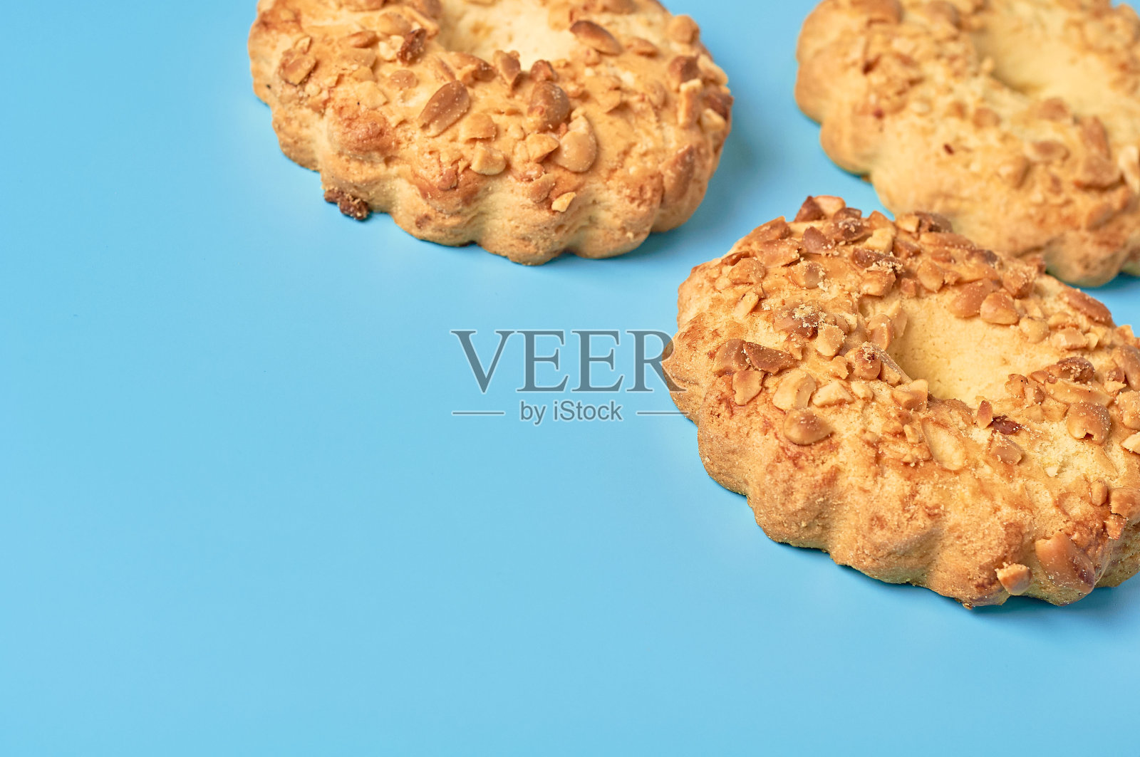 厨房蓝色的桌子上放着三块新鲜的带洞和花生的圆燕麦饼干。空间的文本照片摄影图片