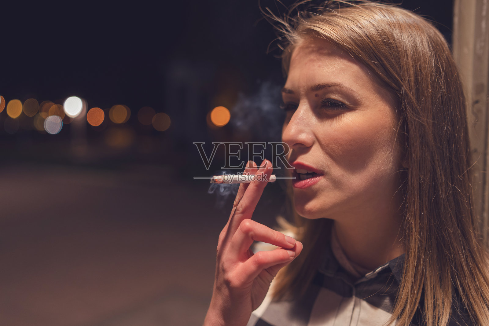 特写年轻的白人女性吸烟者在街道上吸烟的夜晚与城市户外禁烟照片摄影图片