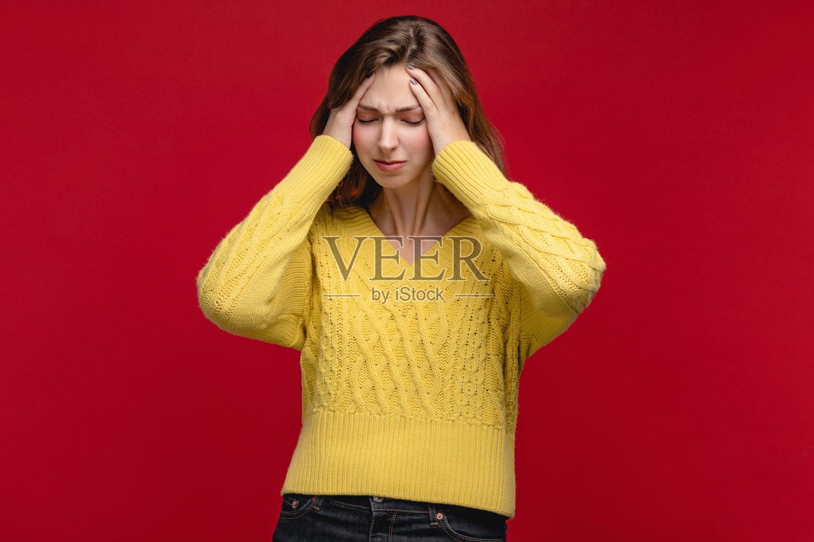 红色背景工作室里穿着黄色套头衫的年轻白人女性，她看起来很悲伤、恼火，可能生病了照片摄影图片