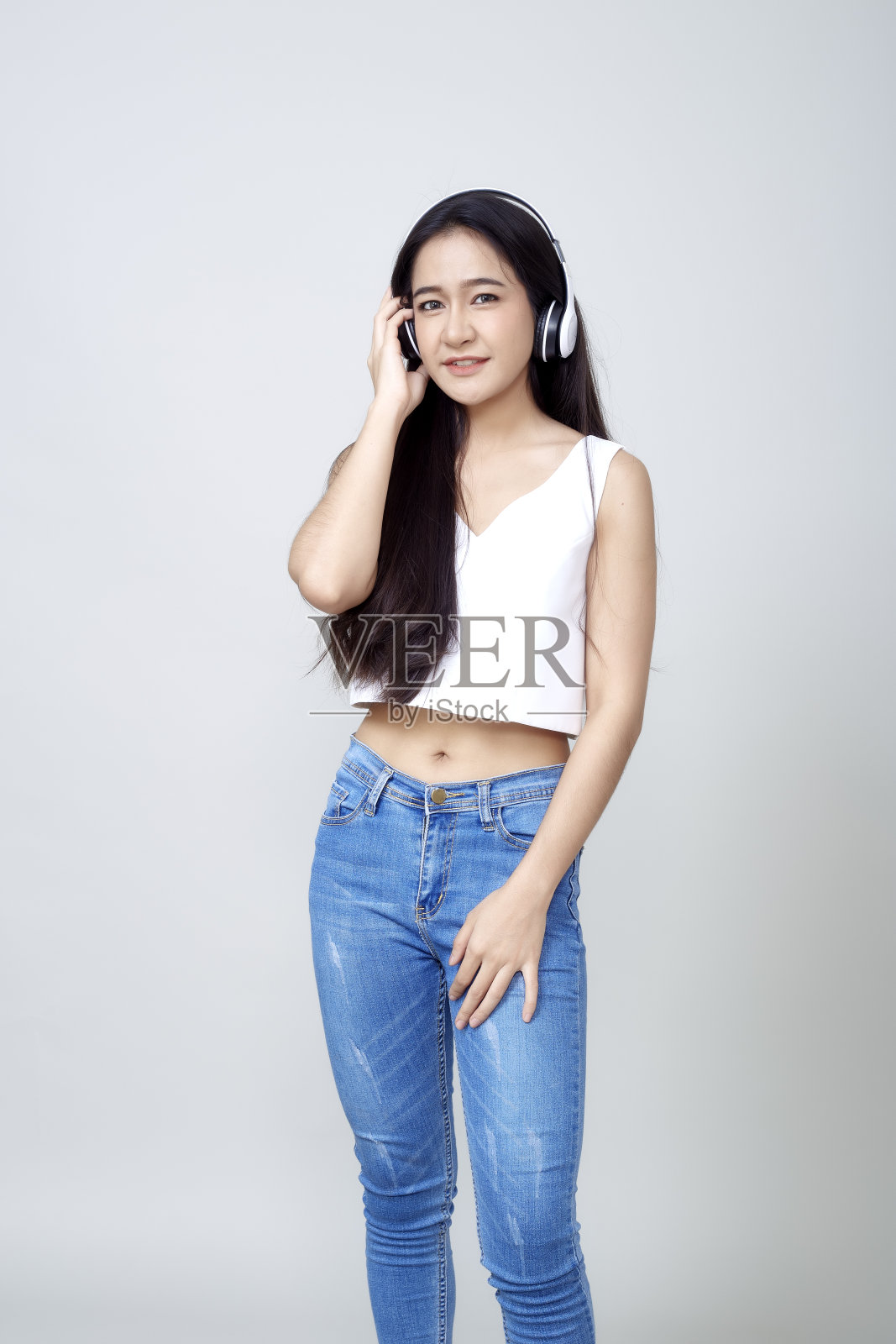 年轻的亚洲女人黑发长发微笑着听音乐与耳机隔离亮灰色背景照片摄影图片