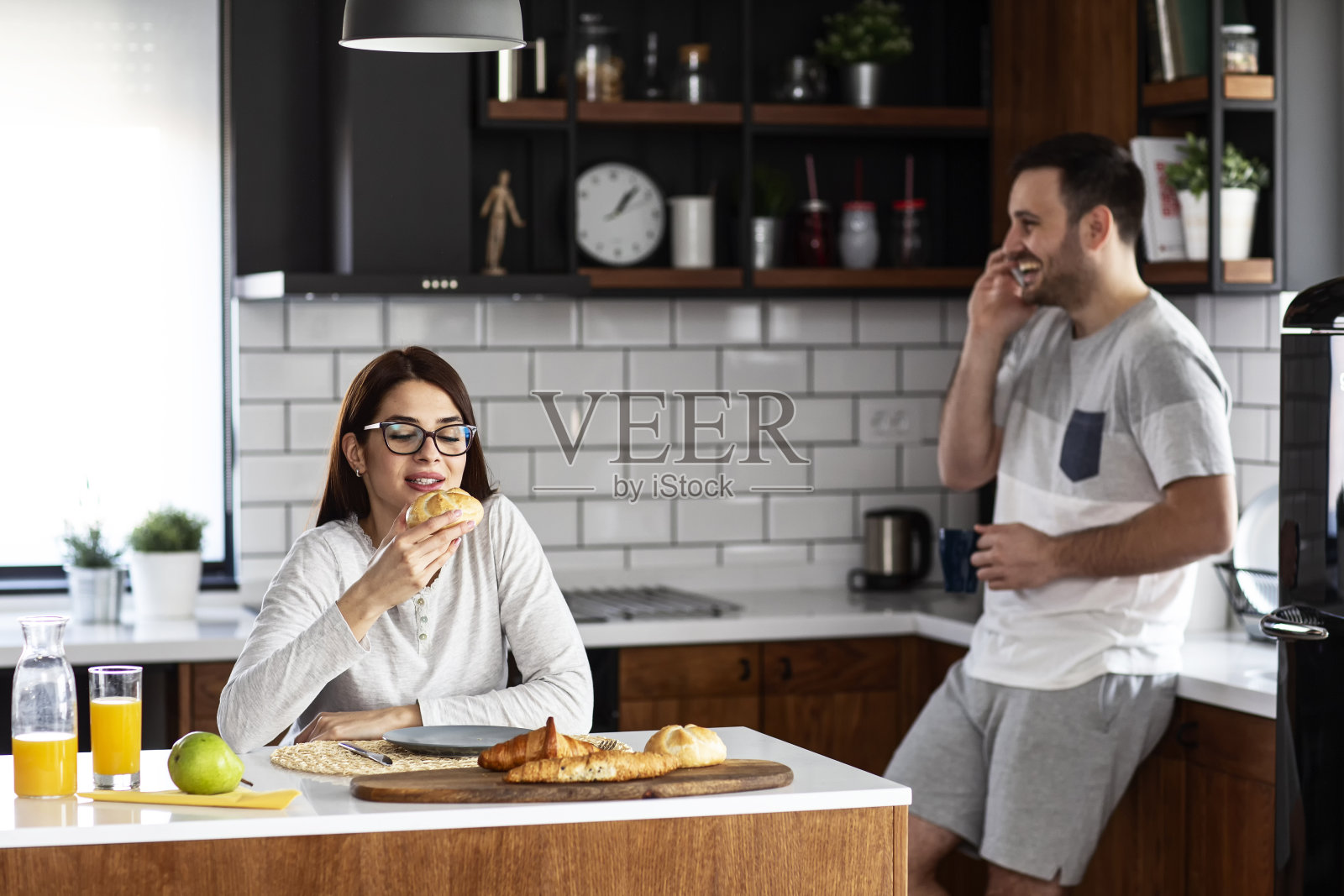 一对夫妇在厨房吃早餐，桌上放着果汁和糕点，他在打电话，而她在喝橙汁照片摄影图片