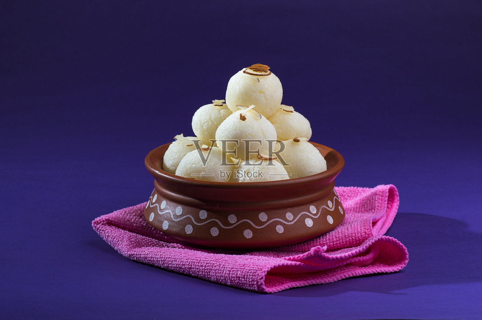 印度甜或甜品——拉斯古拉，著名的孟加拉甜，在粘土碗里，蓝色的餐巾在紫罗兰色的背景上照片摄影图片