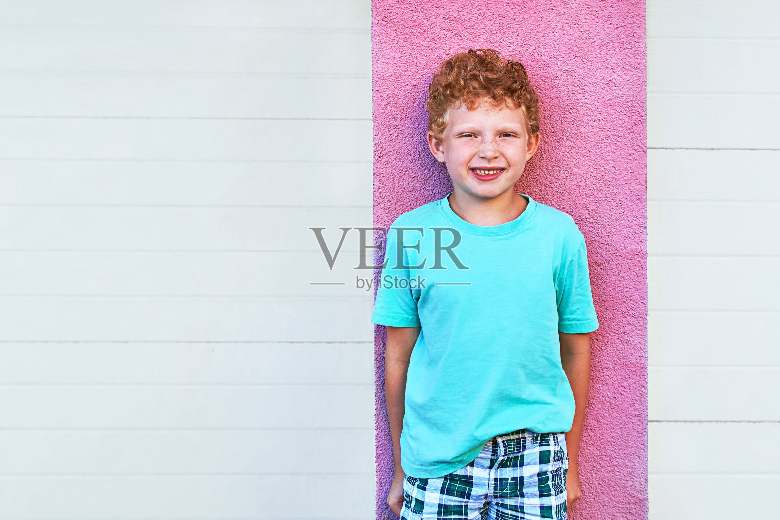 可爱的红卷发男孩微笑着站在墙的背景上照片摄影图片