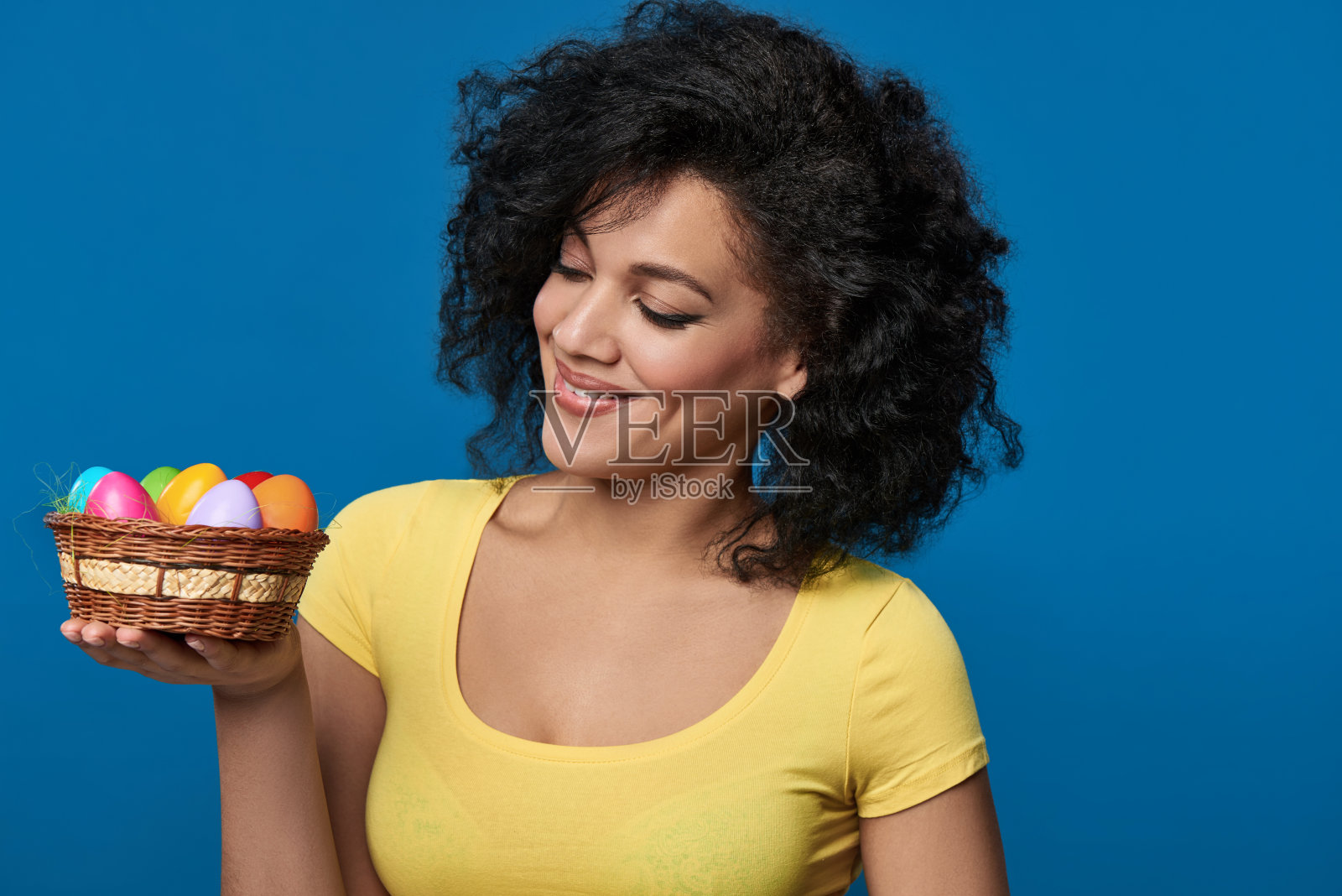 微笑的女人拿着一个篮子，里面有五颜六色的复活节彩蛋照片摄影图片