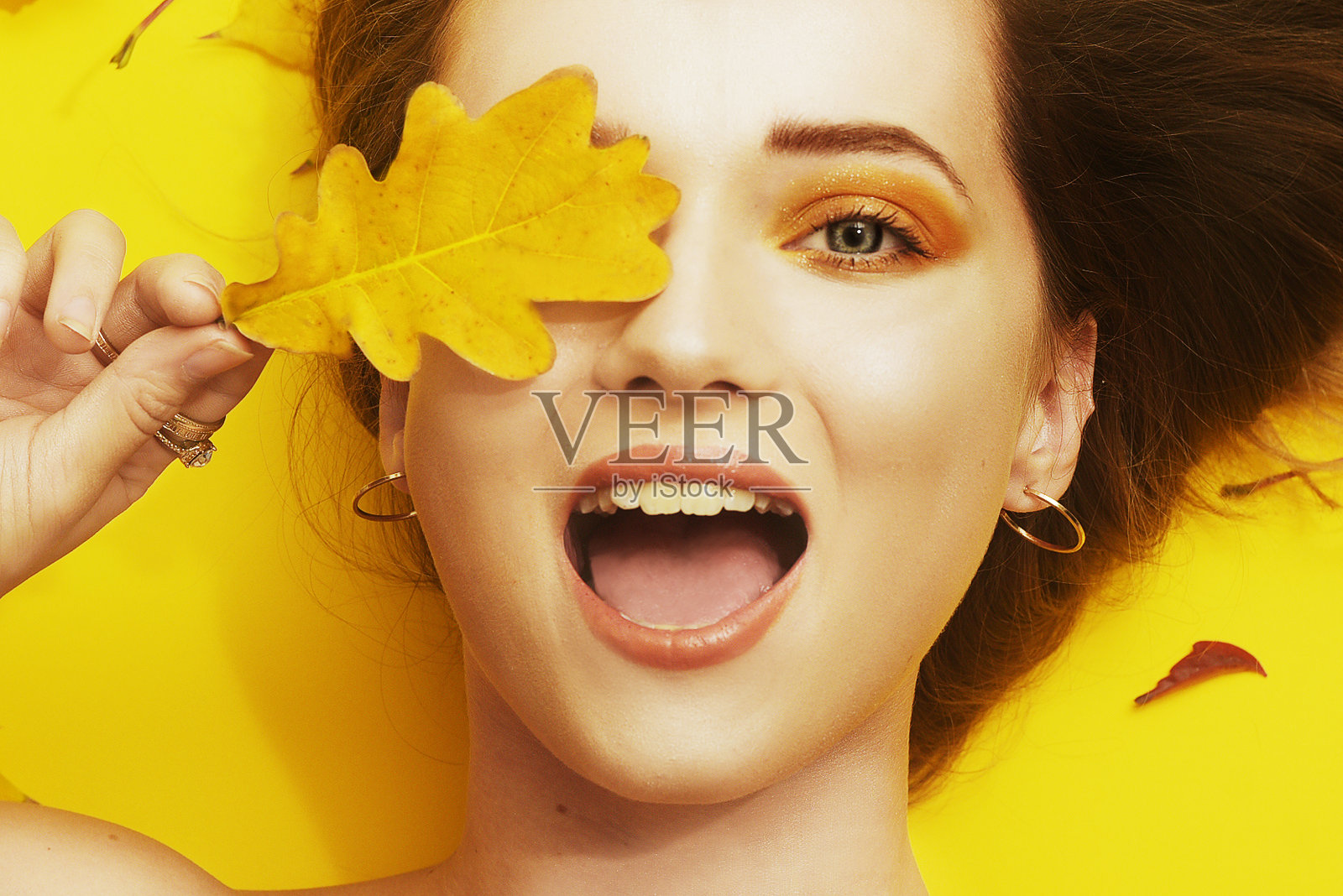 快乐女孩的秋季照片。女孩手持秋叶闭着眼睛微笑。秋季特惠，明亮秋季照片。秋季黄色/橙色妆容。金色耳环，金色秋季。照片摄影图片