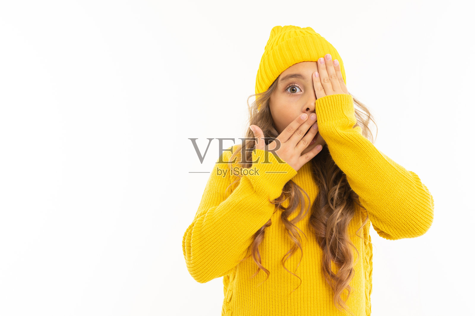 欧洲迷人的女孩在一个黄色的帽子和夹克覆盖她的脸与她的手和看着一只眼睛在一个白色的背景copyspace照片摄影图片