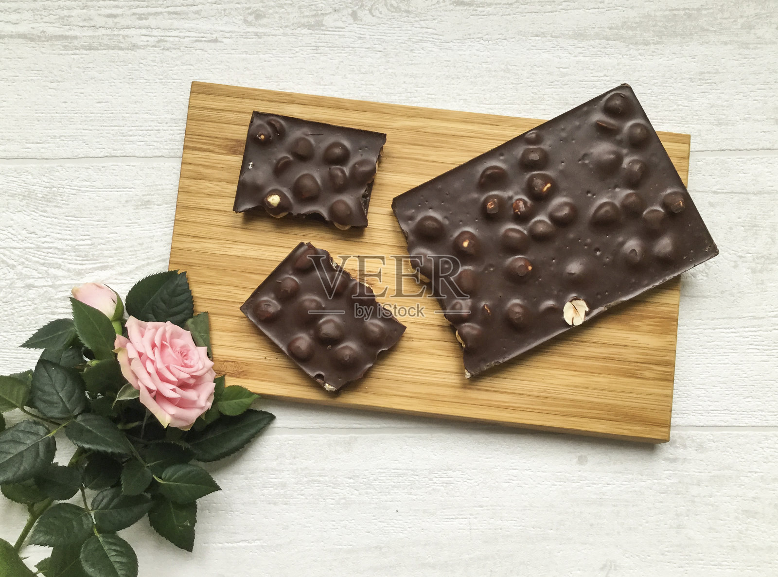 木板上平躺着一块碎巧克力，还有一朵粉红色的玫瑰照片摄影图片