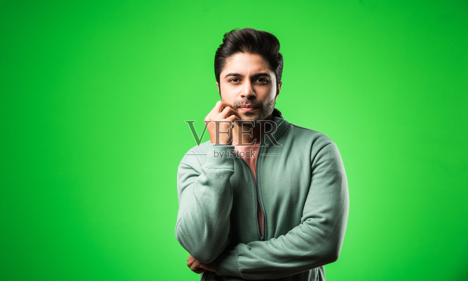 焦虑的印度/亚洲男子站在绿色背景前，神情紧张照片摄影图片
