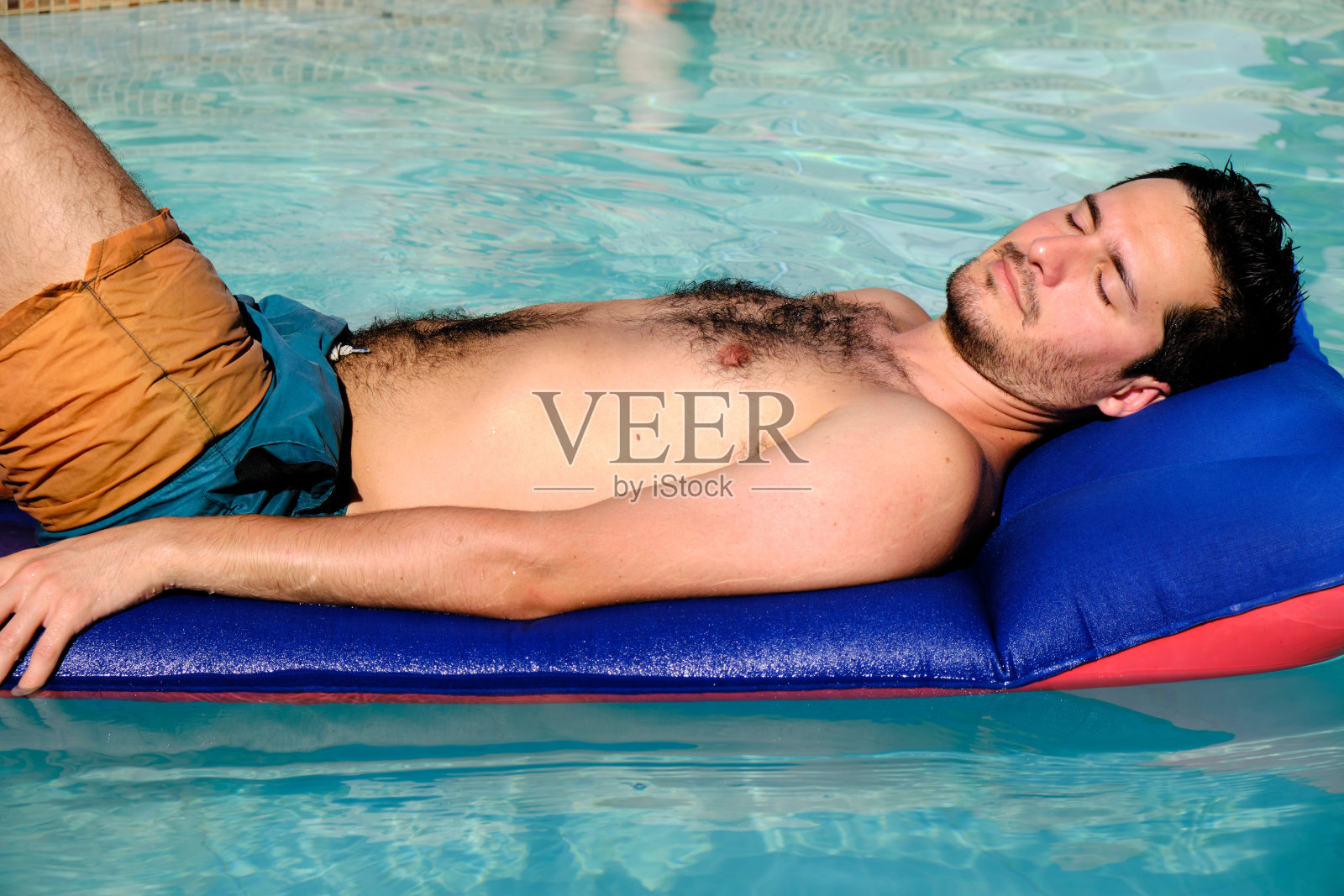 一个穿着泳衣坐在水垫上的英俊青年照片摄影图片