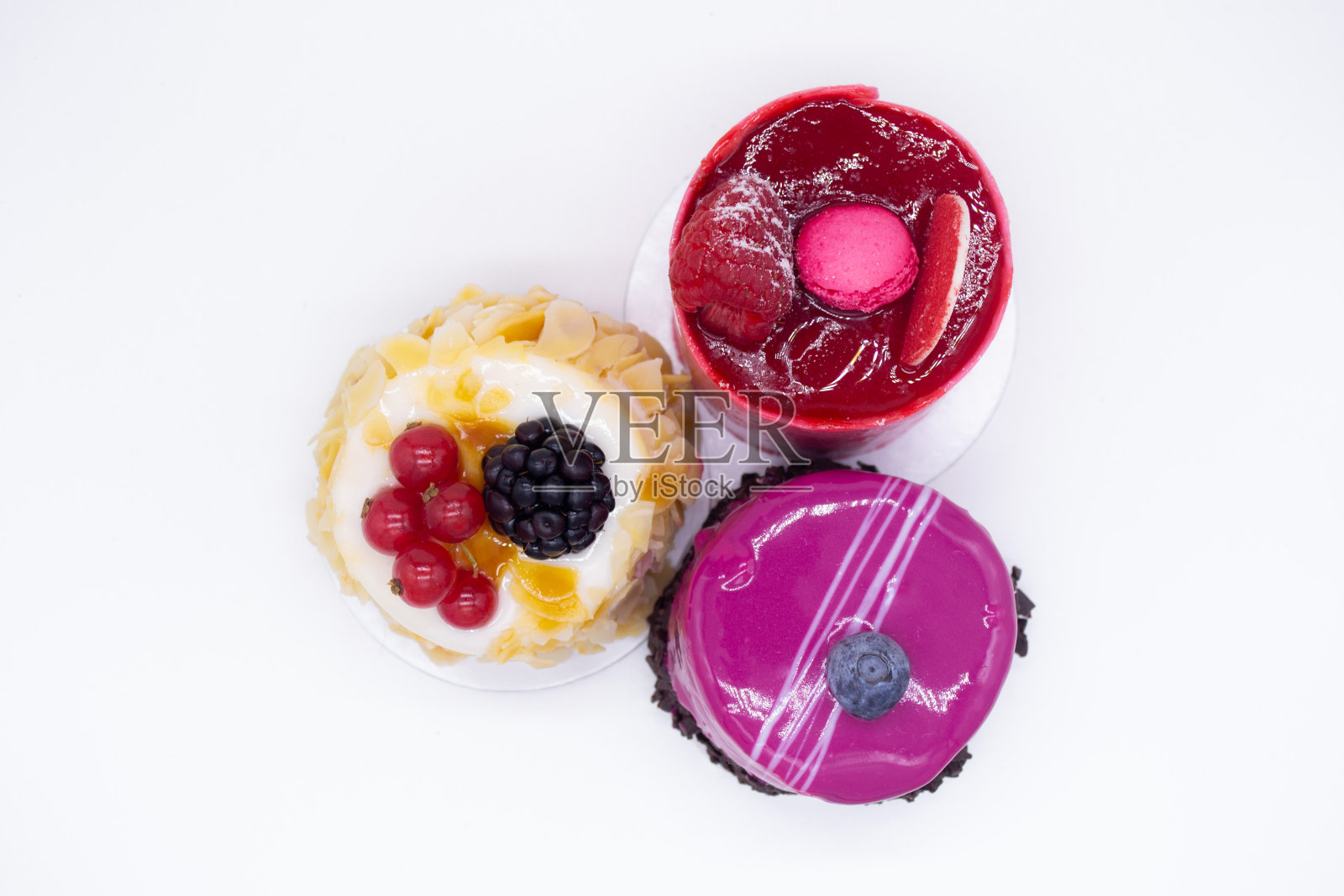 白色背景上的三个蛋糕:鲜红的覆盆子，上面是杏仁蛋白杏仁饼，奶油蛋糕上有杏仁花瓣，红醋栗和黑莓，粉色慕斯上有蓝莓和巧克力片照片摄影图片