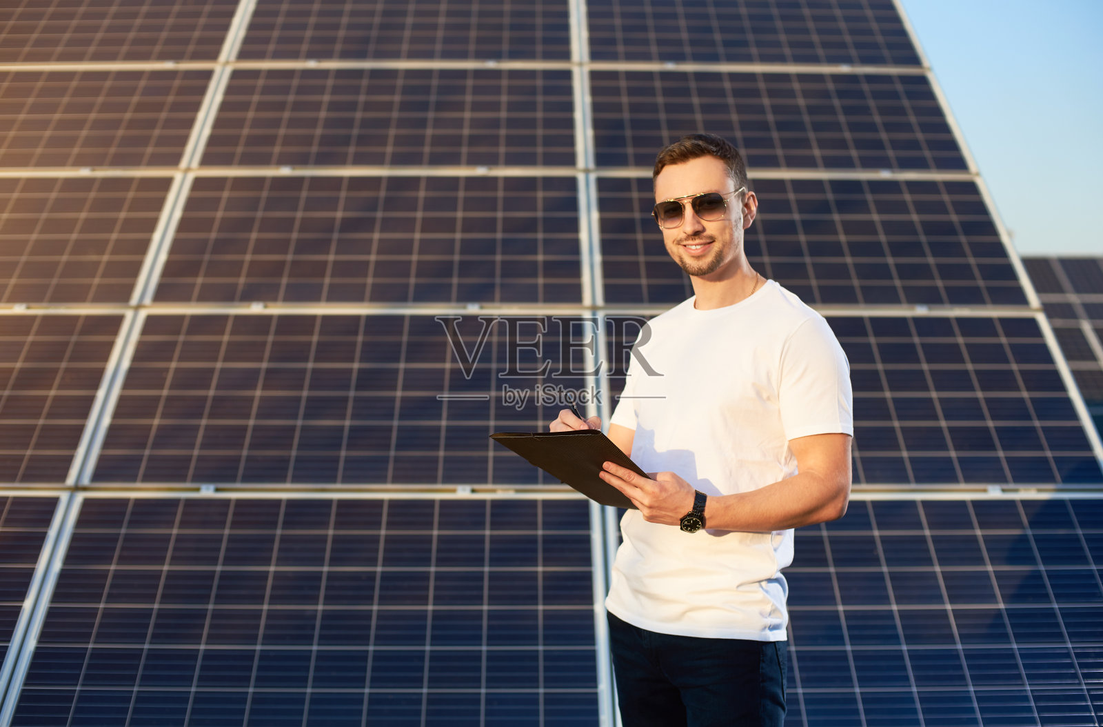 英俊男士手拿文件夹和笔，背景是温暖的太阳能电池板照片摄影图片