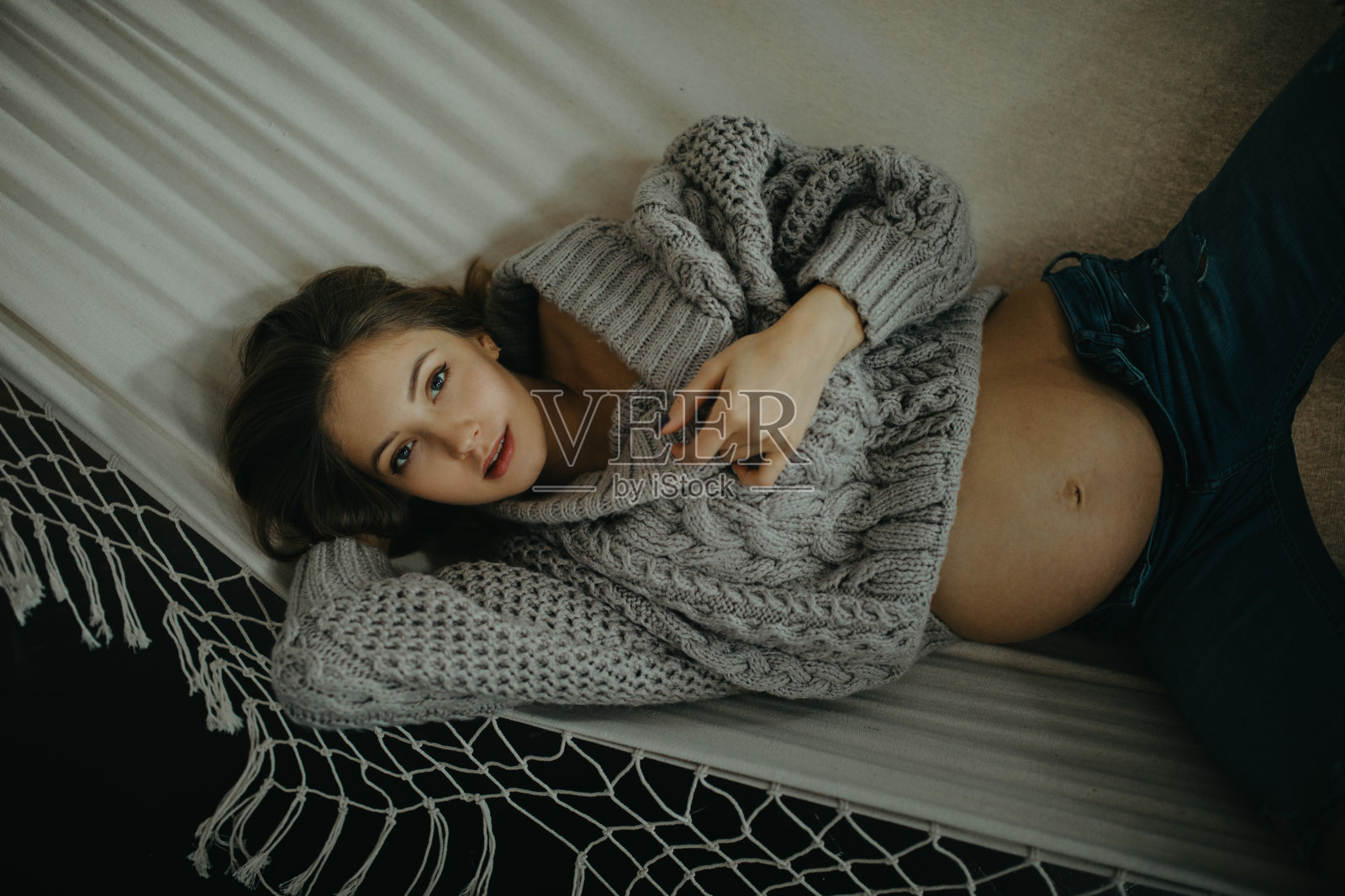 穿着套衫和牛仔裤的孕妇在吊床上休息。照片摄影图片