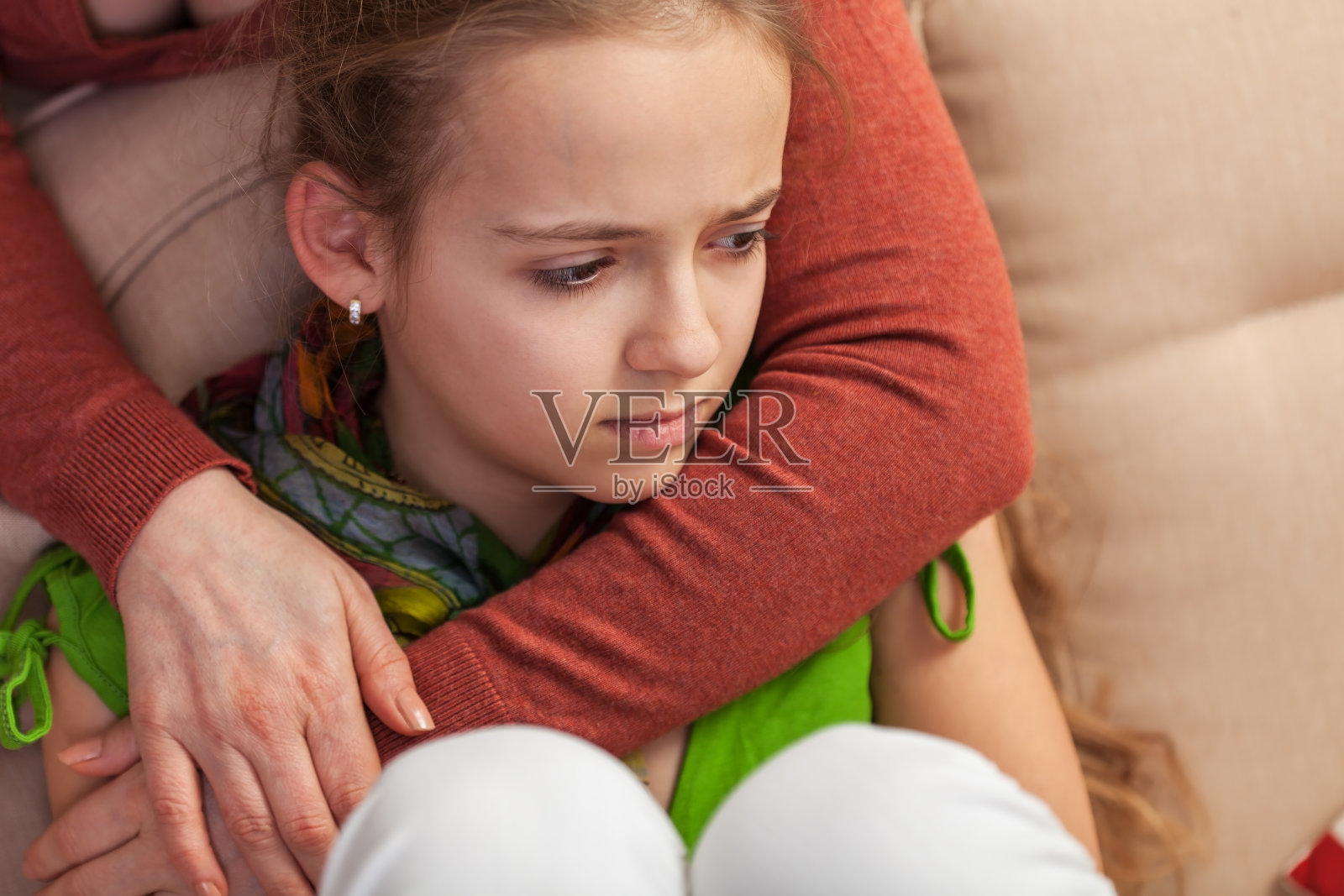 一位忧伤的年轻女孩坐在沙发上，一位女士拥抱并安慰她照片摄影图片