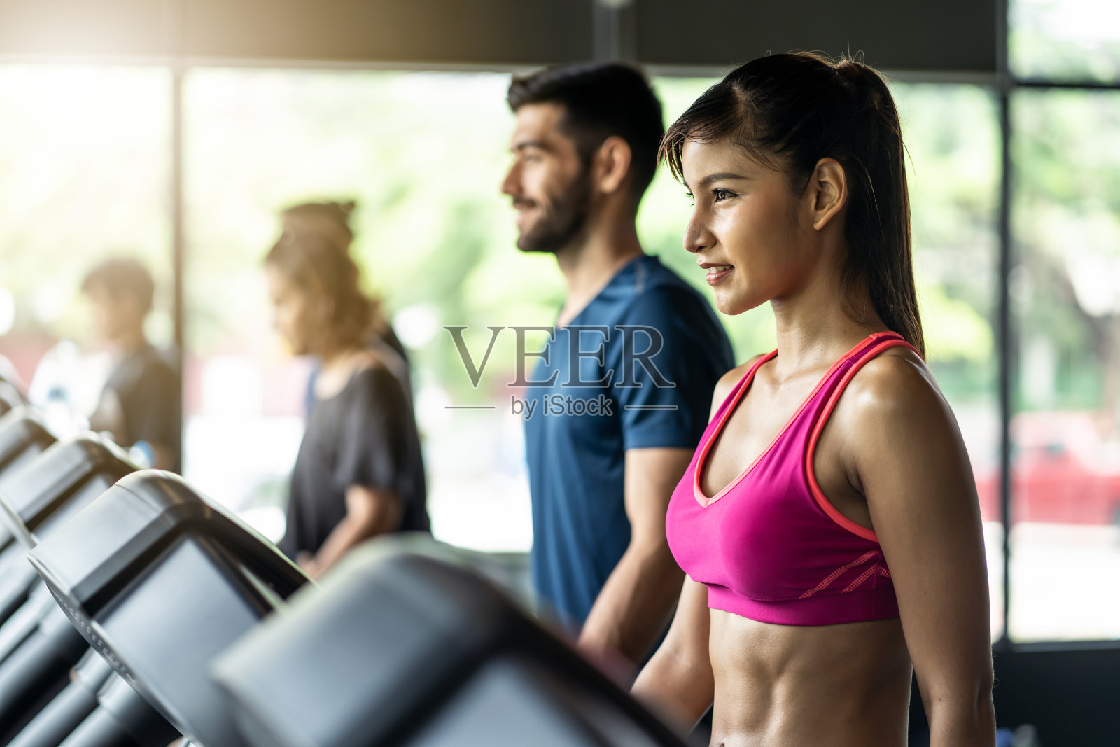 年轻貌美的亚洲女人和英俊的白人男人在现代健身房里的跑步机上或跑步机上行走。在健身房锻炼和健身照片摄影图片