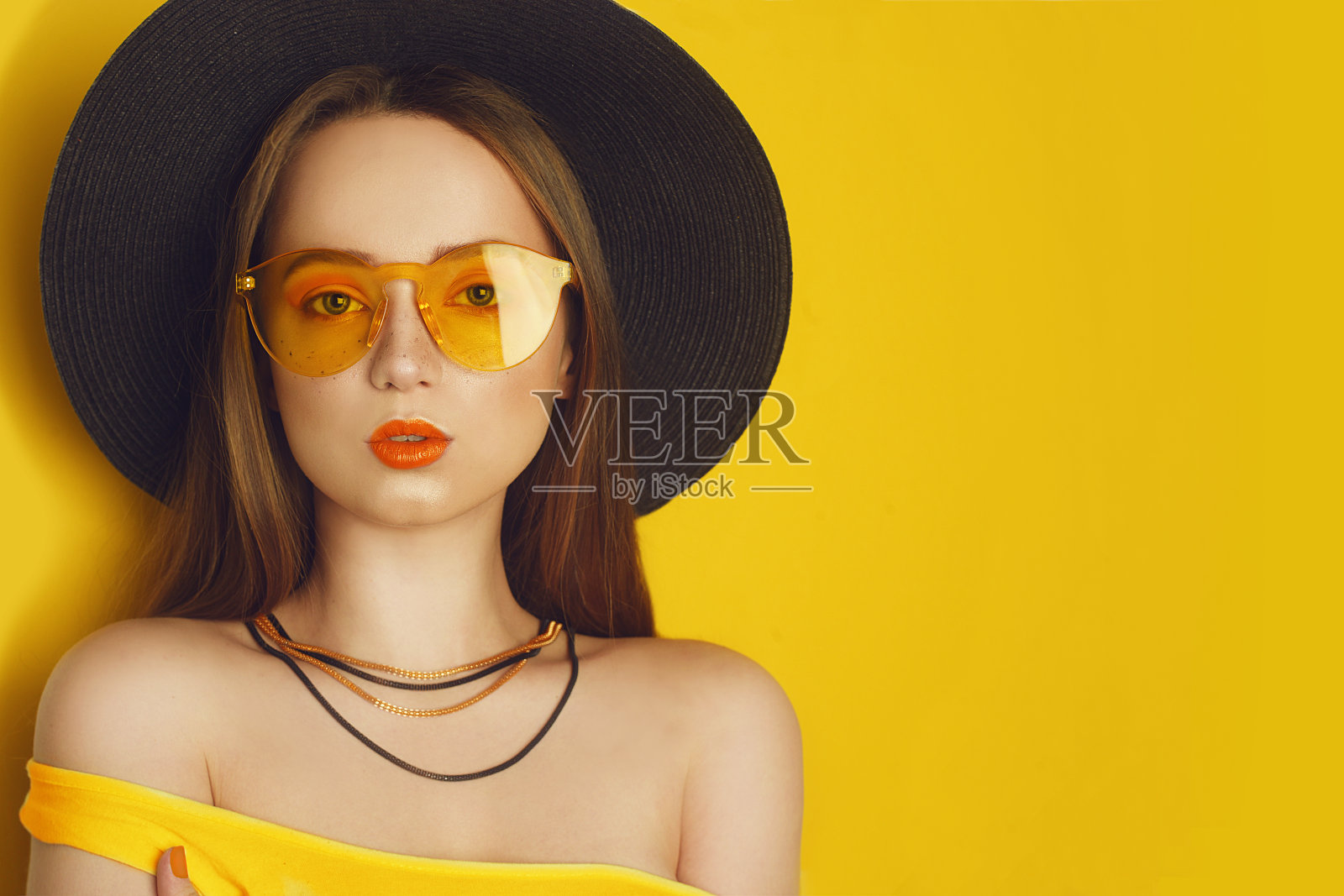 橙色时尚配饰美女模特，留长直发的时尚女性，潮流妆容，橙色背景，戴黑色大帽子和黄色太阳镜的女孩，留白照片摄影图片