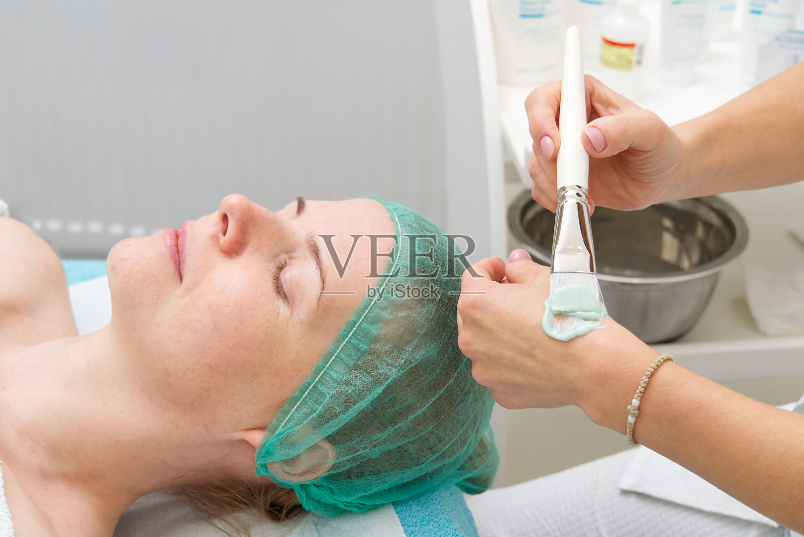 美容师给年轻美丽的女士敷上天然保湿面膜。用刷子涂抹脸部的抗老化和皱纹面膜。美容的概念。美容师用这个程序来清洁面部有问题的皮肤。照片摄影图片