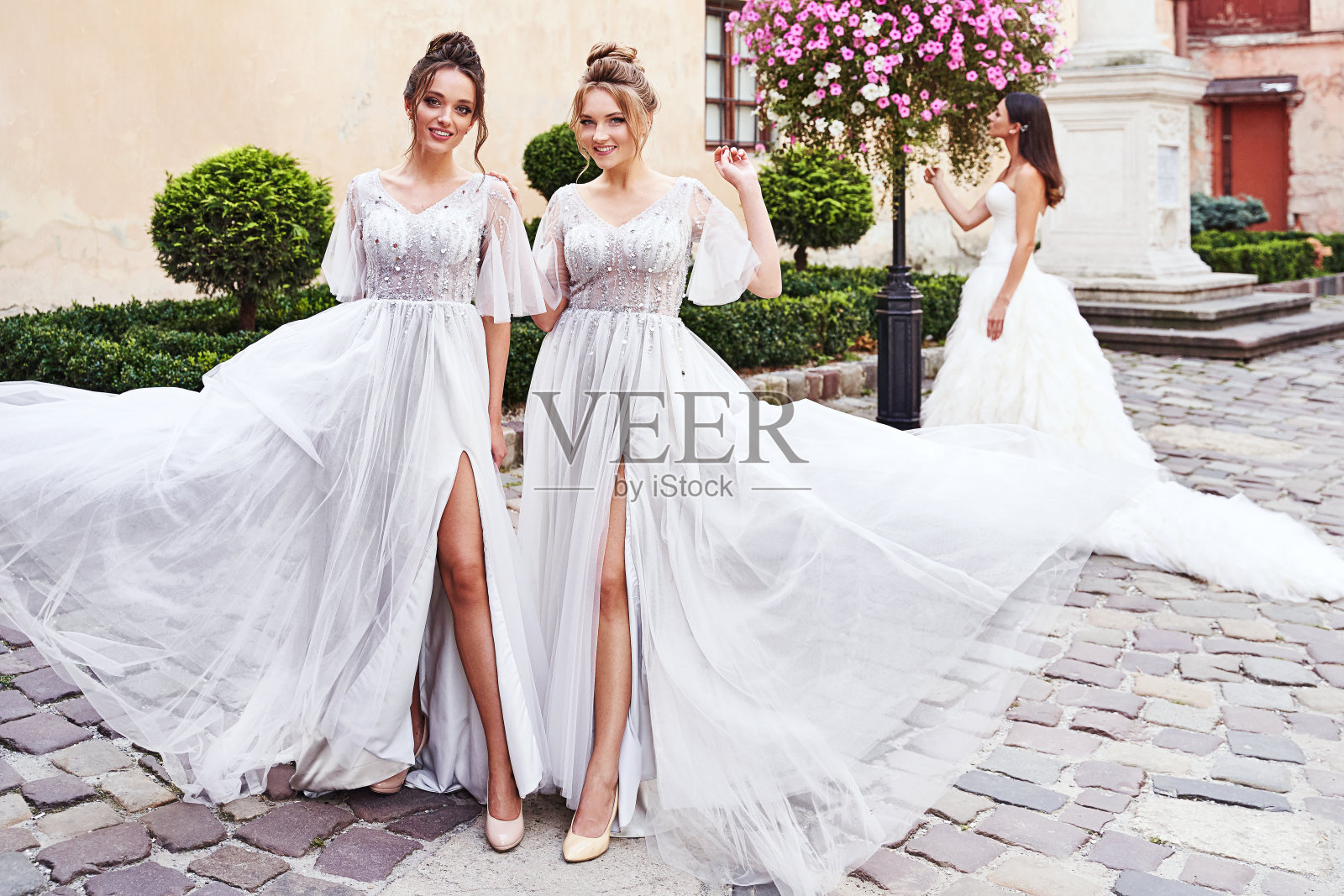 美丽的新娘和伴娘在一个美丽的古老的欧洲城市在一个婚礼的日子里，华丽优雅时尚的浅灰色银色地板长裙。照片摄影图片
