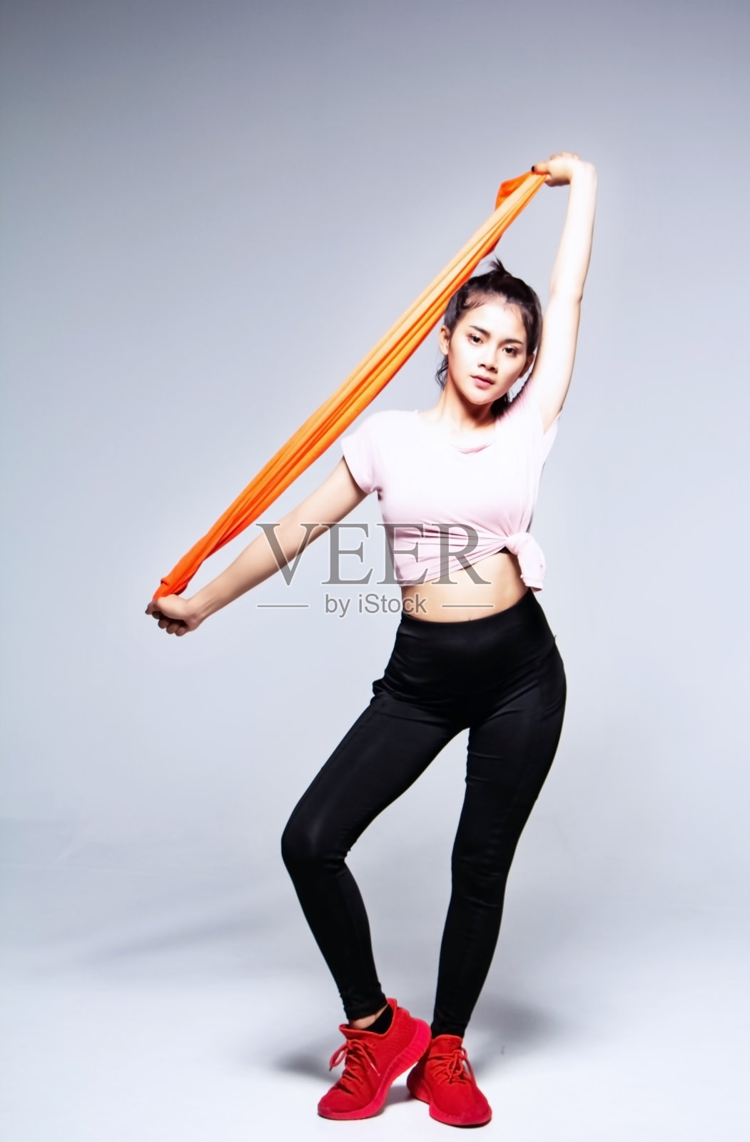 穿着运动服的女人拉着橙色毛巾，脚尖朝下，在工作室摆出舞蹈基本姿势照片摄影图片