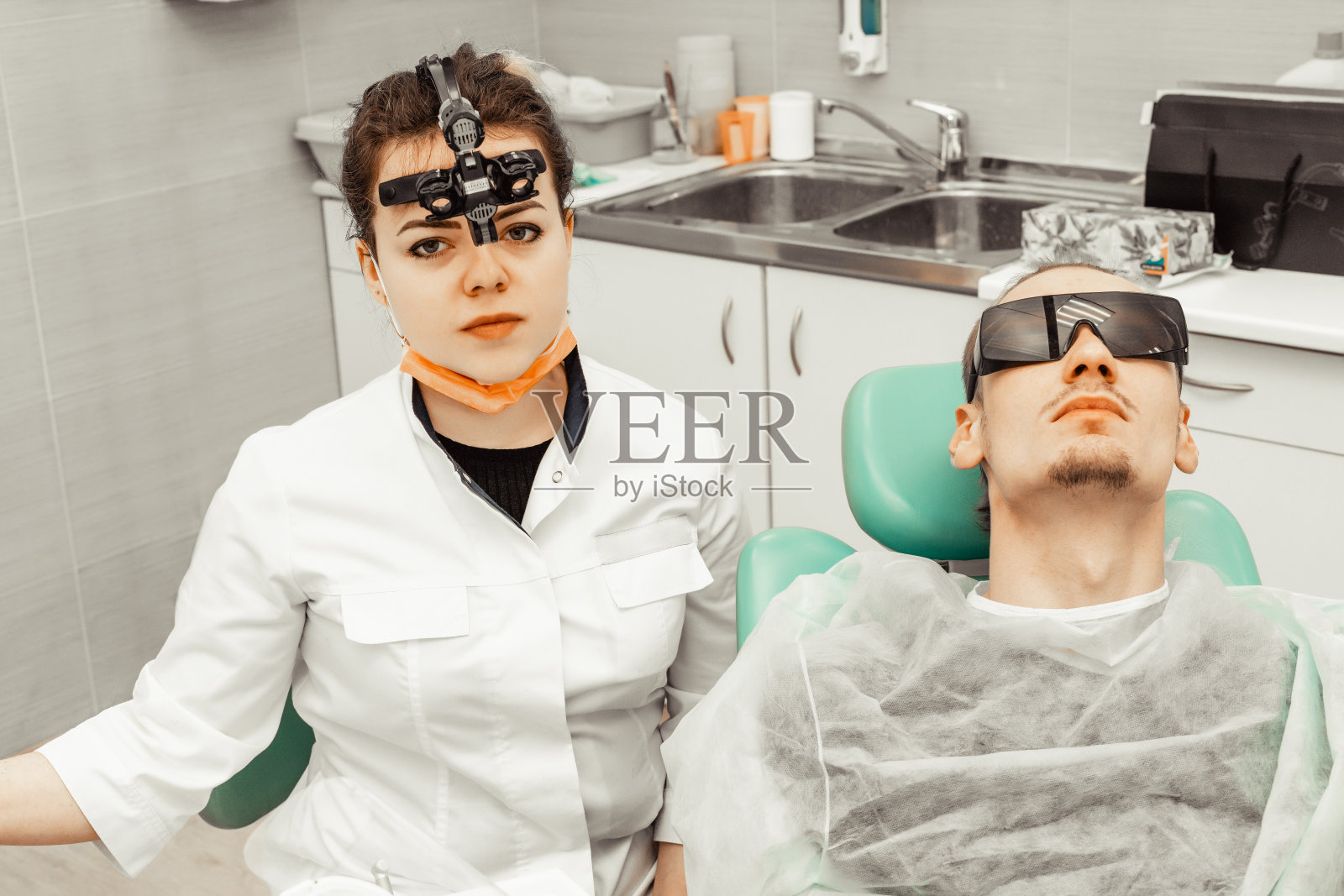 年轻女牙医为男患者治疗，医生使用一次性手套、口罩和帽子照片摄影图片