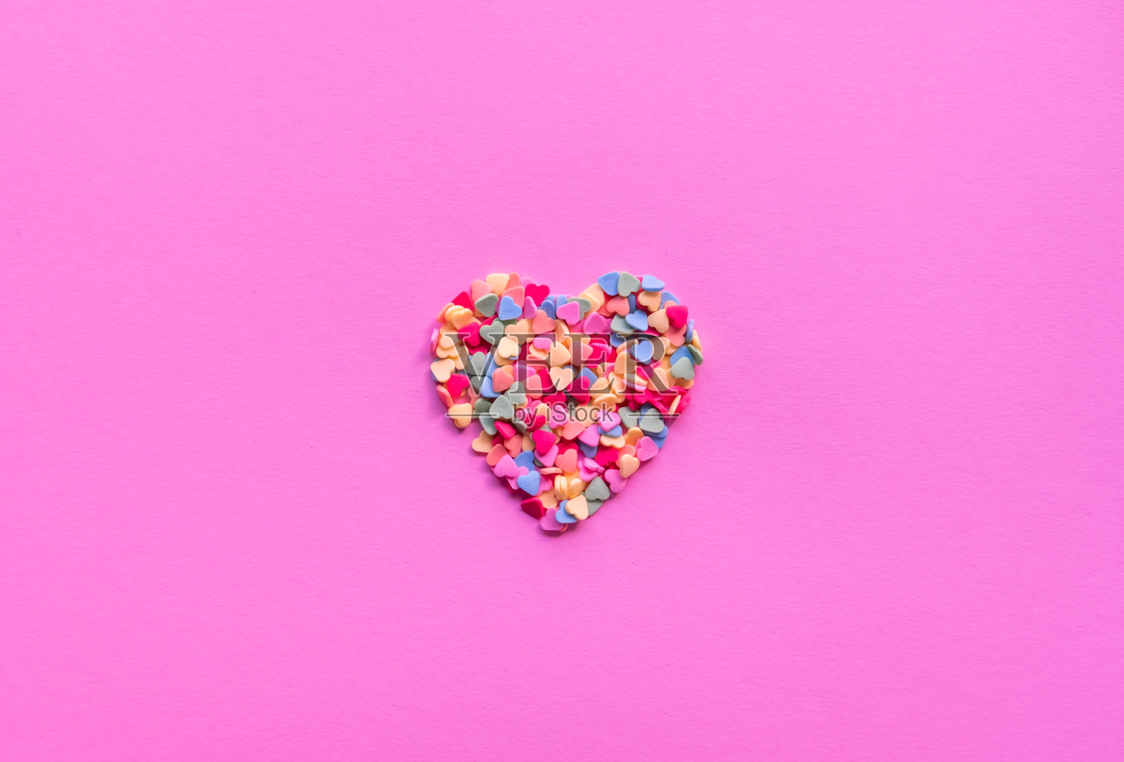 鲜艳的粉红色背景上点缀着五颜六色的糖心形状。情人节的概念。照片摄影图片