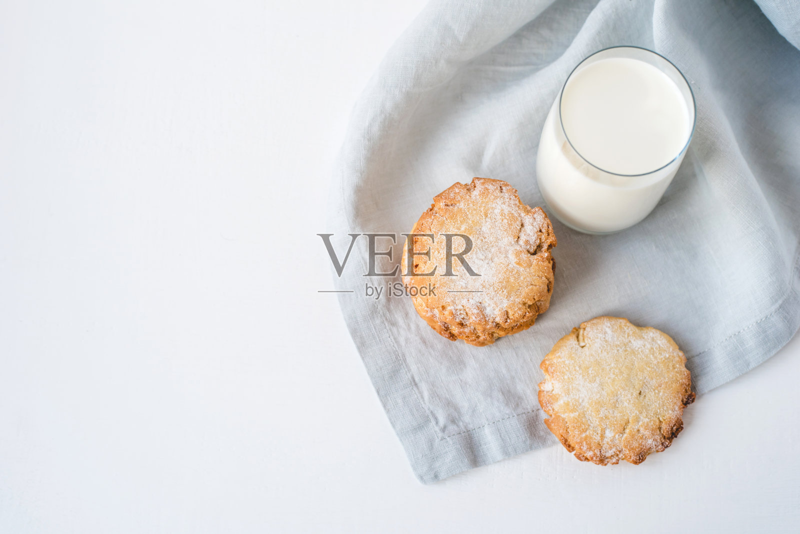 把饼干堆在一块亚麻布餐巾上，还有一杯牛奶。照片摄影图片