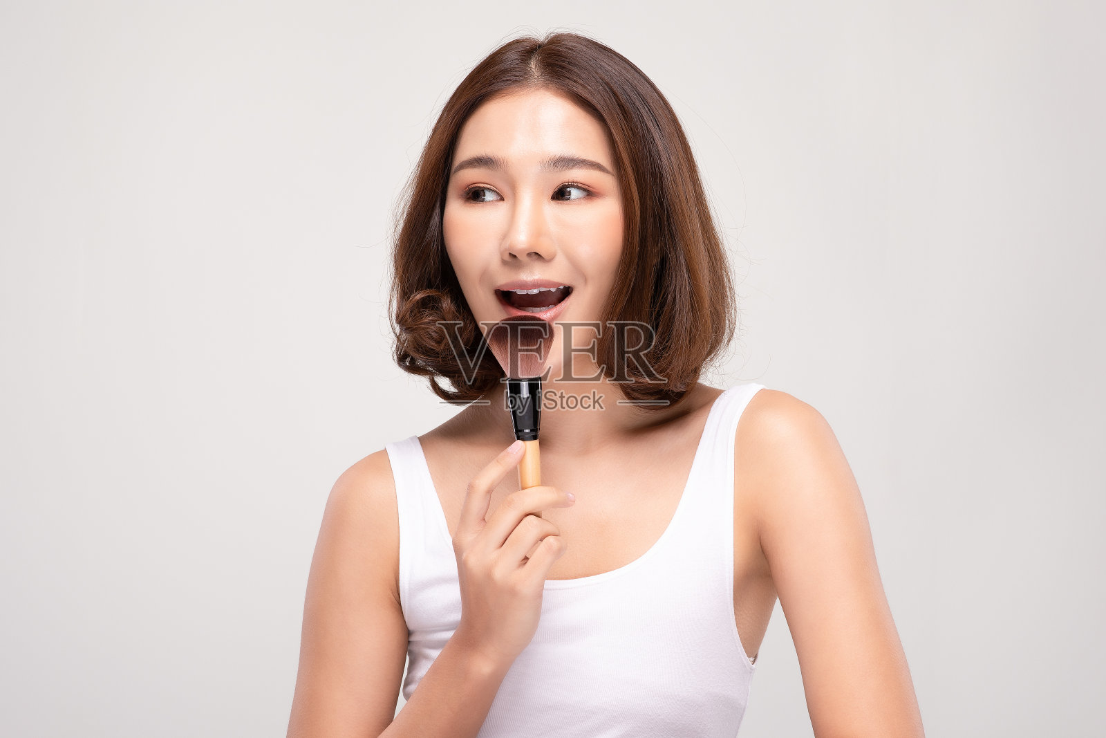 手持化妆刷，拥有健康肌肤的快乐亚洲年轻女性照片摄影图片