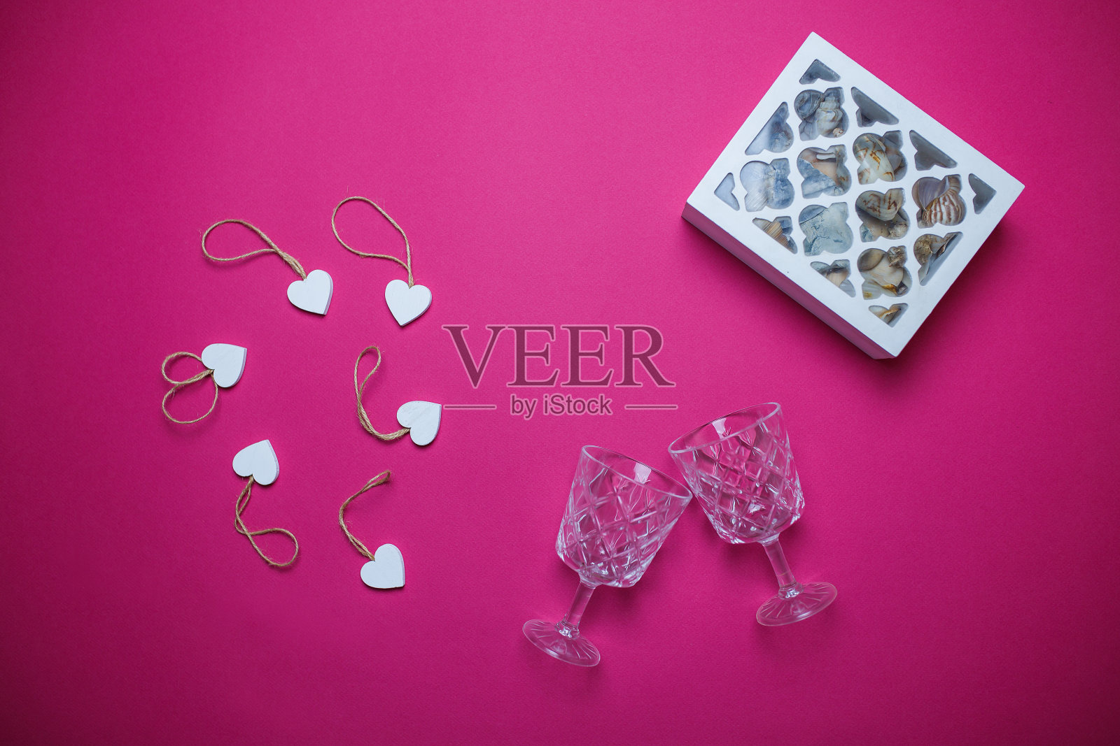 小的白色木制心和白色木制首饰盒在粉红色的背景与复制空间。情人节卡片，粉红色背景上有两个酒杯。照片摄影图片