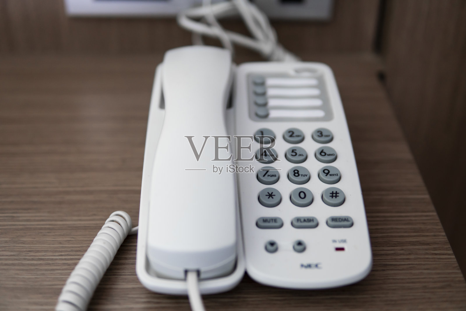 酒店里棕色的桌子上放着一台白色老式电话，灰色的底座。照片摄影图片