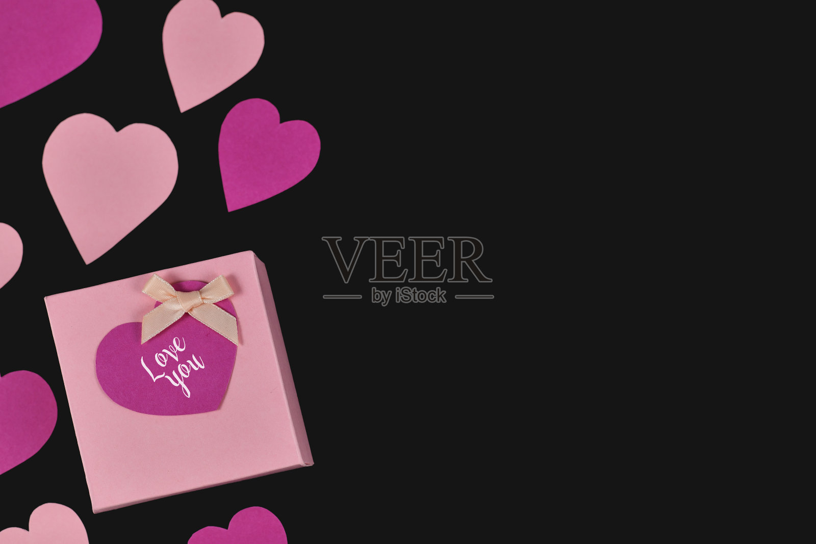 浪漫的情人节公寓放着一个粉红色的小礼盒，黑色的背景上写着“爱你”，还有心形和空白的拷贝空间照片摄影图片
