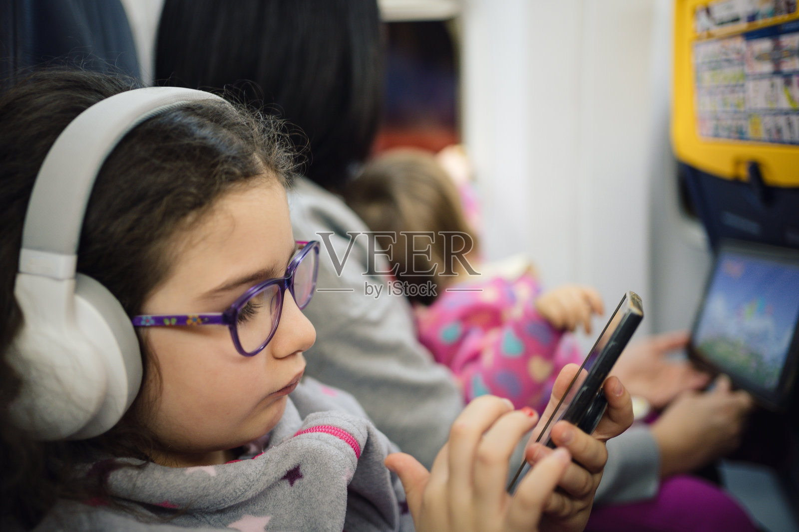 小女孩在飞机上玩手机游戏。照片摄影图片