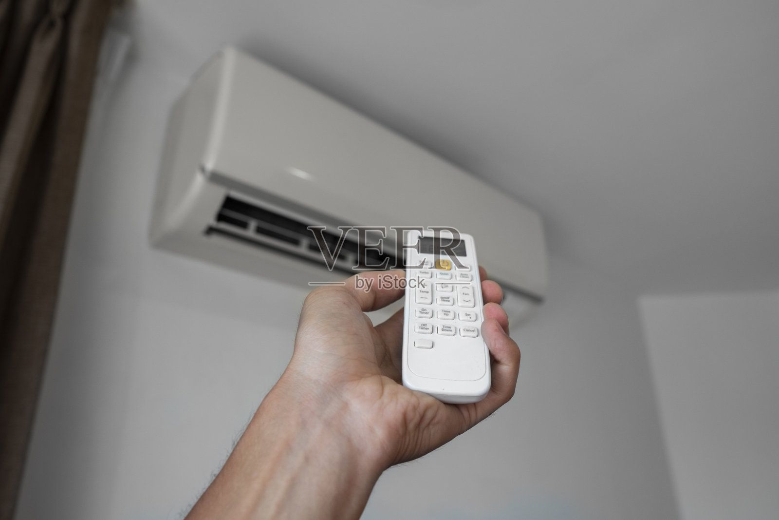 男人使用遥控器。手持遥控器调节安装在白色墙壁上的空调温度。室内舒适温度。健康概念和节能。照片摄影图片
