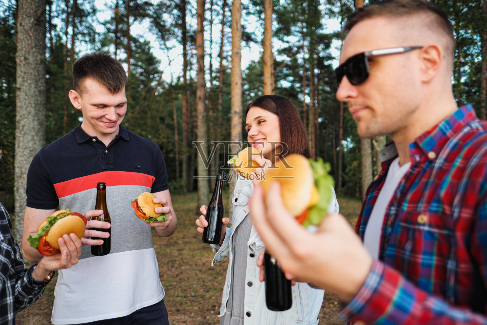 一群朋友在大自然中休息放松。人们吃汉堡，喝啤酒，交流和欢笑。照片摄影图片