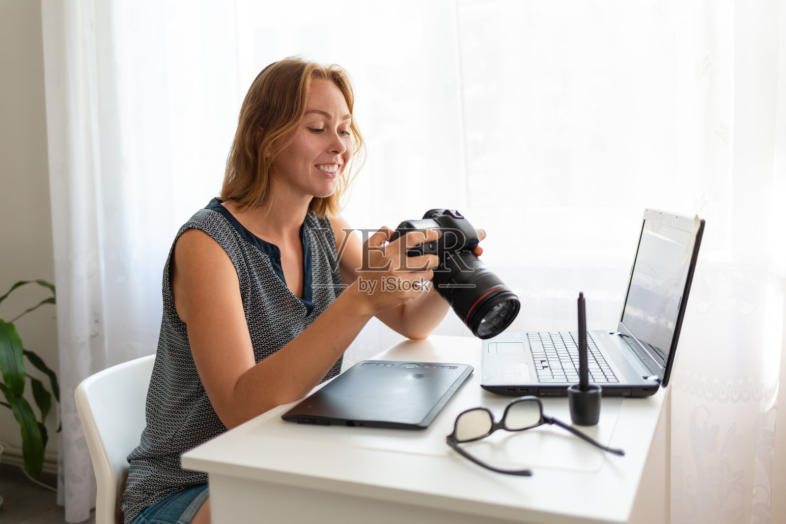 坐在桌前用相机工作的年轻女摄影师照片摄影图片