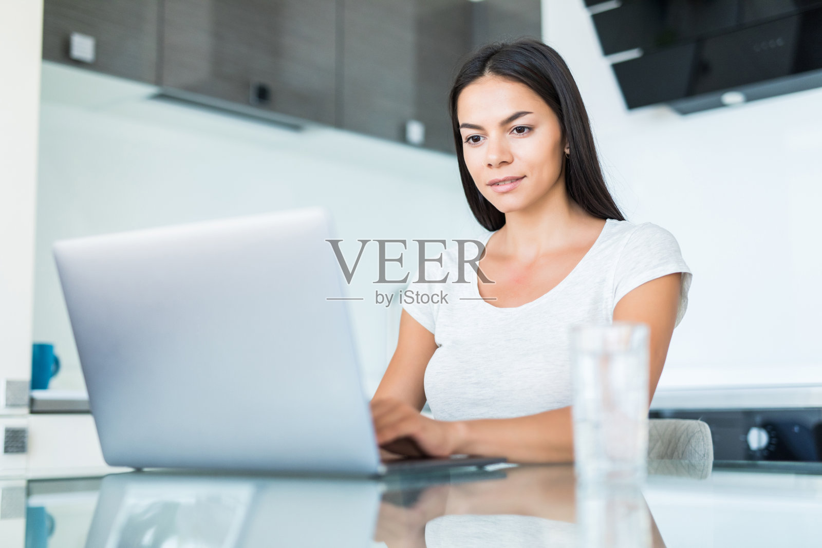 快乐的年轻女子在厨房的柜台上使用笔记本电脑照片摄影图片