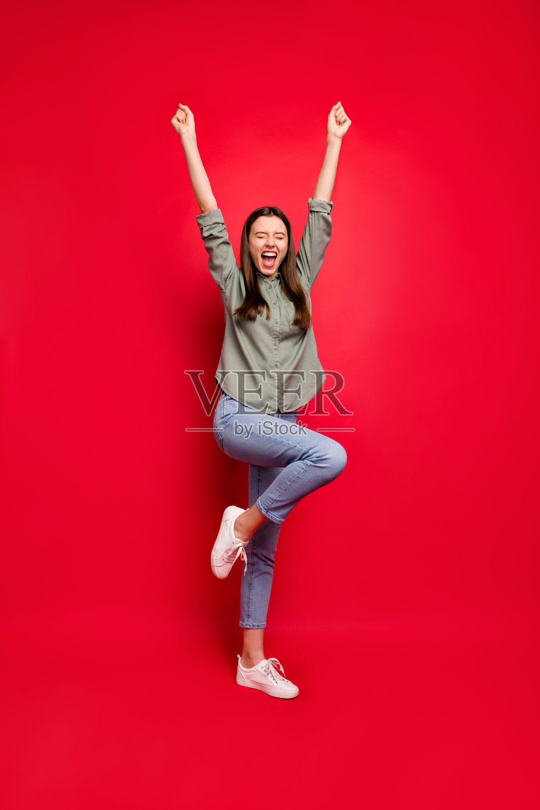 全身垂直的照片疯狂的女士举起拳头庆祝体育比赛胜利，欢呼尖叫穿休闲的灰色绿色衬衫牛仔裤孤立的红色背景照片摄影图片