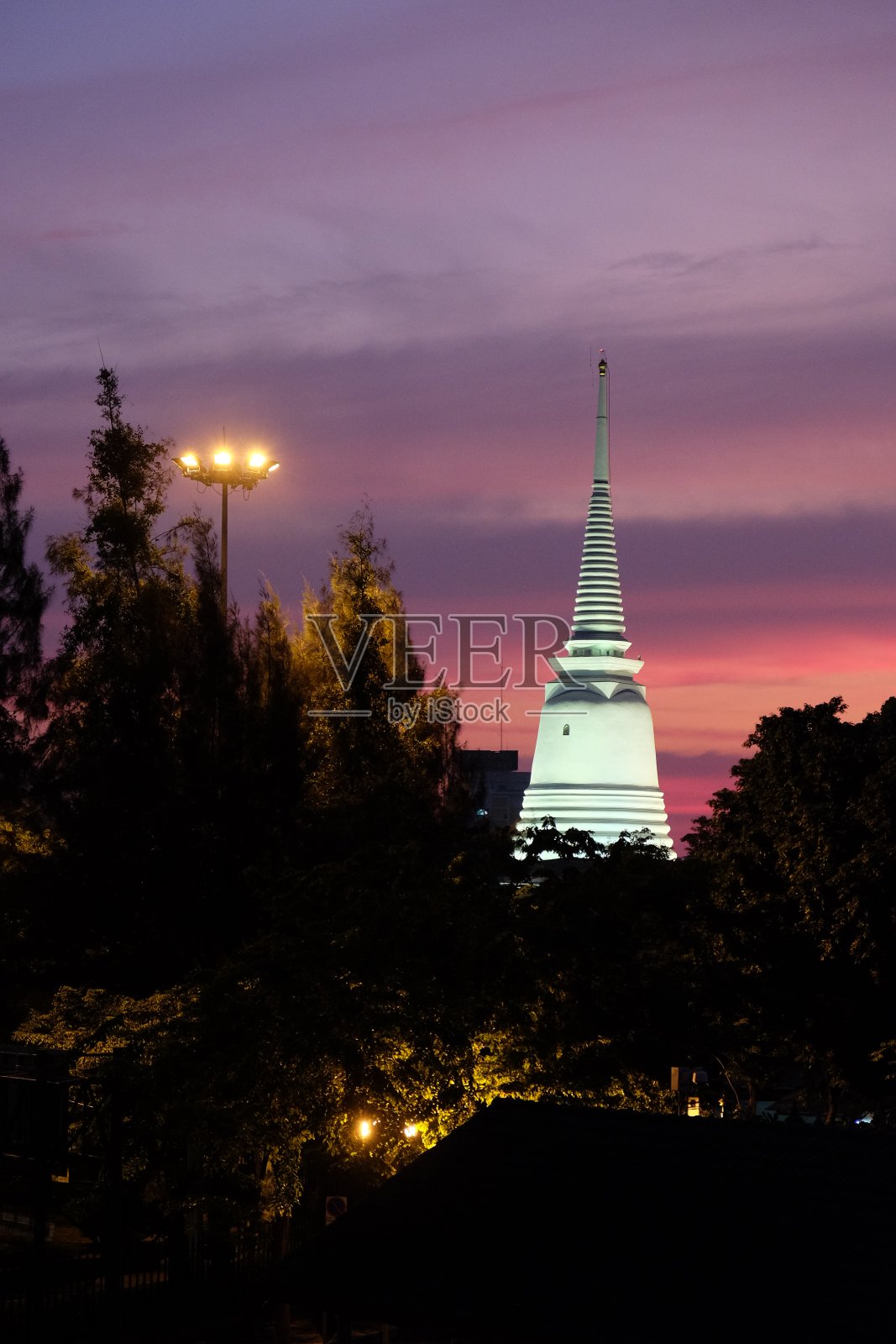 美丽的日落映衬着树木的剪影。一座佛教寺庙被点燃的尖顶。照片摄影图片