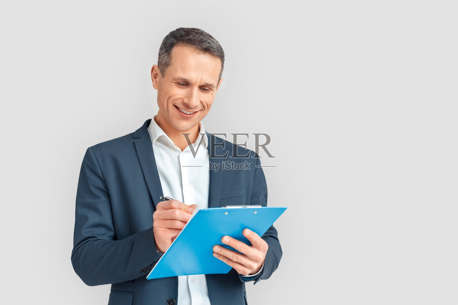 中年商人在白色背景前做笔记，面带微笑照片摄影图片