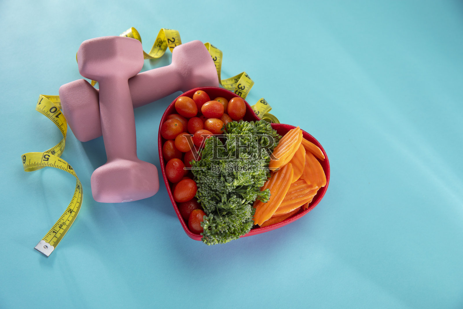 蔬菜在一个心碗，哑铃和一个苹果在蓝色的背景照片摄影图片