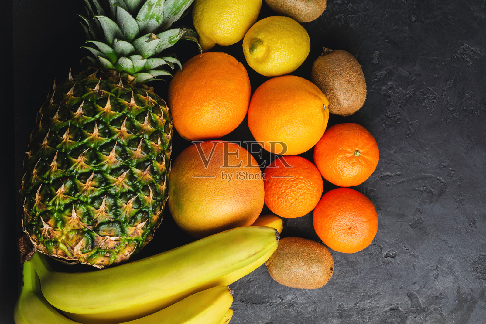 各种热带水果，香蕉，猕猴桃，橙子，橘子，柠檬，菠萝，葡萄柚在黑暗的背景，俯视图，拷贝空间照片摄影图片