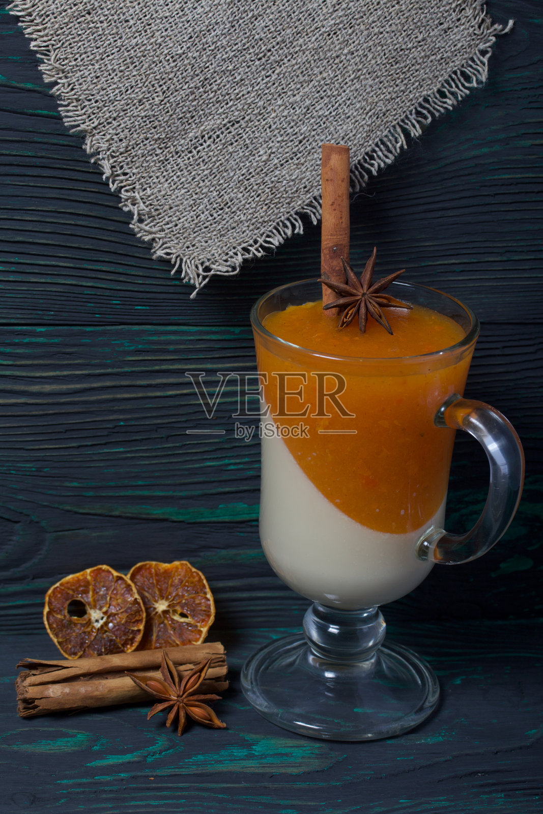 玻璃高脚杯里有两层果冻。奶油和橘子果冻。附近是装饰用的香料。在拉丝板的表面涂上黑色和绿色。照片摄影图片