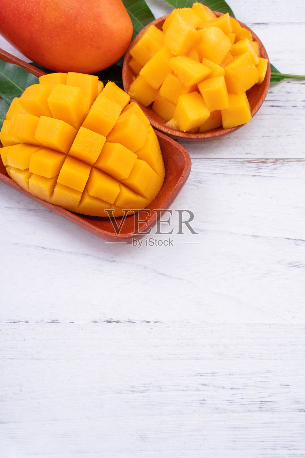 新鲜的芒果，美丽的切好的水果和绿色的叶子在明亮的木桌的背景。热带水果设计理念，拉近距离，复制空间。照片摄影图片